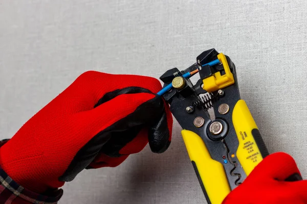 Kırmızı eldivenli bir elektrikçi elektrik kablolarındaki yalıtımı kaldırmak için tel kesiciler kullanıyor..