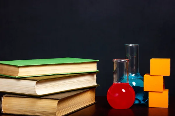 Chemical glassware with liquid, test tubes and books on a wooden table. Scientific research. School or student desk.