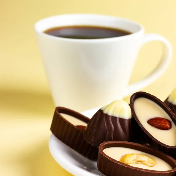 Čokoládové bonbóny a šálek kávy na žlutém pozadí. Formát čtverce — Stock fotografie