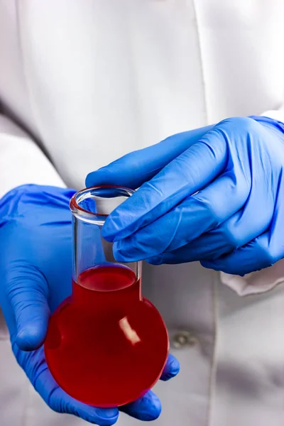 Mavi eldivenli bir eczacı kırmızı bir sıvıyla kimyasal bir şişe tutuyor.. — Stok fotoğraf