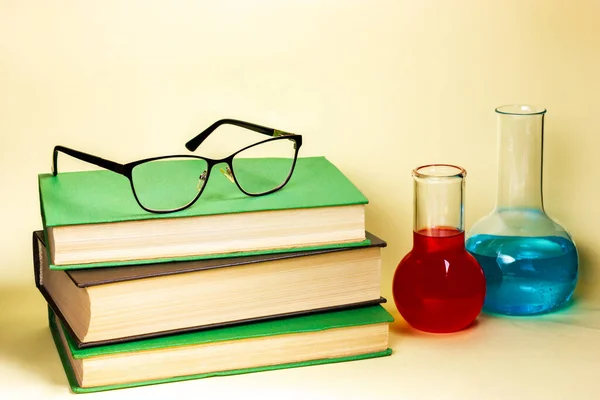 Glasses for sight lie on a pile of books, chemical dishes are nearby. — Stock Photo, Image
