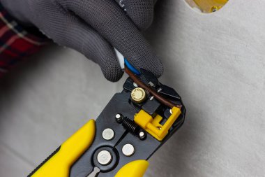 Bir elektrikçi elektrik kablolarını söker. Sarı tel kesiciler elektrik kablosu yalıtımını soyar.