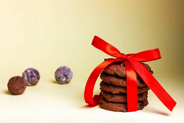 Un piccolo regalo sotto forma di biscotto legato con un nastro rosso e qualche tartufo al cioccolato su fondo giallo. — Foto Stock