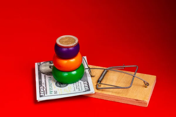 Долларовая купюра и пирамида с монетами евро в мышеловке на красном фоне. Финансовая пирамида, финансовое мошенничество. — стоковое фото