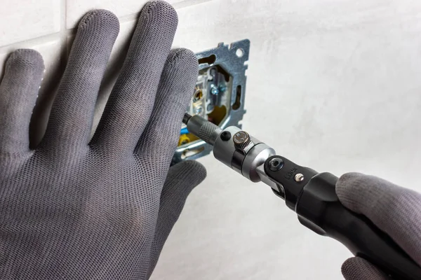 stock image A man in gray gloves uses a screwdriver to install an electrical outlet. Installing an electrical outlet.