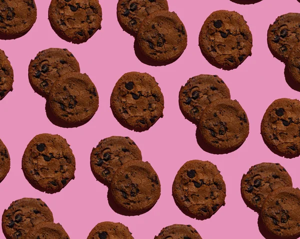 Galletas con chispas de chocolate sobre fondo rosa. Vista superior del patrón sin costuras —  Fotos de Stock