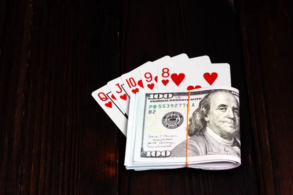 A bundle of dollars tied with an elastic band and a combination of playing cards on a dark wooden table. Lucky win, jackpot. Royal flush in poker. — Stockfoto