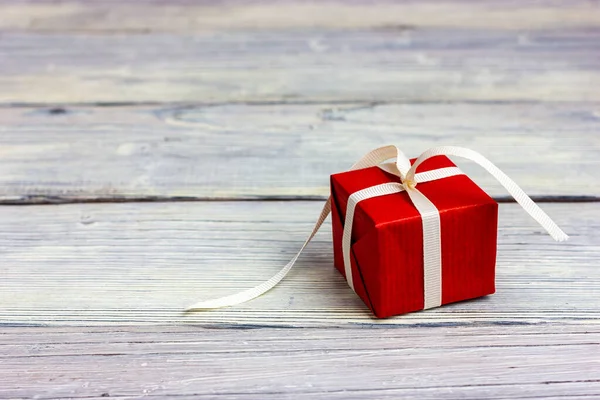 Small red gift with a white ribbon on a light wooden table. — Fotografia de Stock