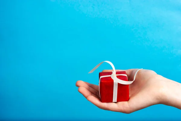 A mão feminina dá um presente vermelho com uma fita branca. Parabéns ao seu ente querido no Dia dos Namorados. Natal, presente de Ano Novo. — Fotografia de Stock