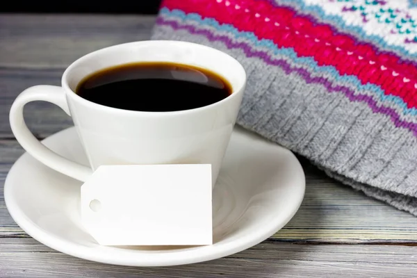 Uma xícara de café e uma etiqueta de papel branco com lugar para texto em uma mesa de madeira leve. — Fotografia de Stock