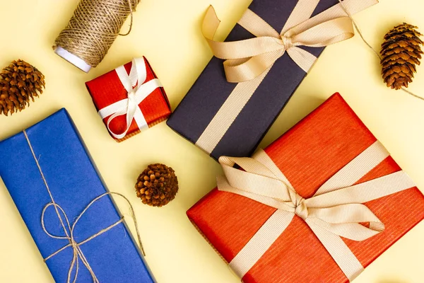 Cadeaux enveloppés dans du papier d'emballage noir, rouge et bleu sur fond jaune. Préparation cadeau vue du dessus. — Photo