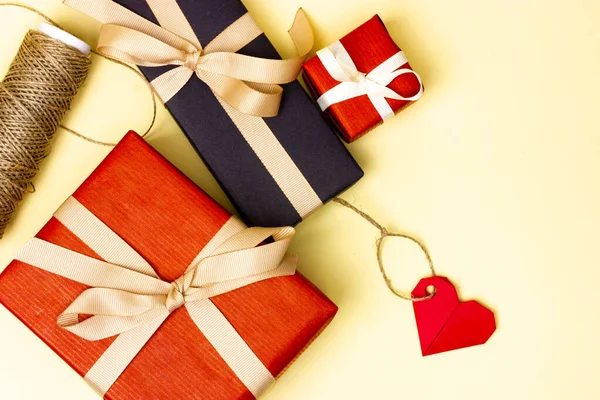 Deux cadeaux enveloppés dans du papier rouge et noir avec un ruban beige sur fond jaune. Emballage cadeau vue du dessus. — Photo