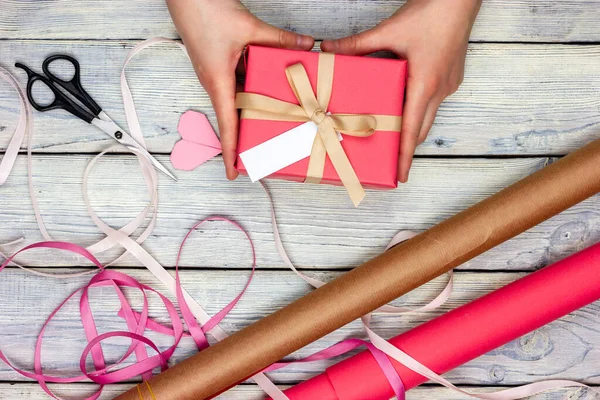 Les mains féminines préparent un cadeau enveloppé dans du papier rose. Processus d'emballage cadeau. — Photo