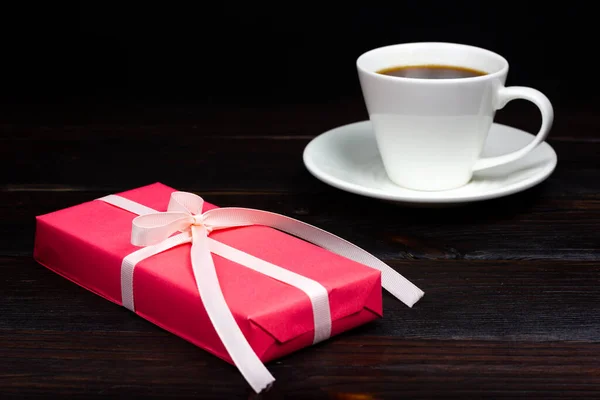 Cadeau rose avec ruban blanc et une tasse de café dans la lumière sombre. Style rustique — Photo