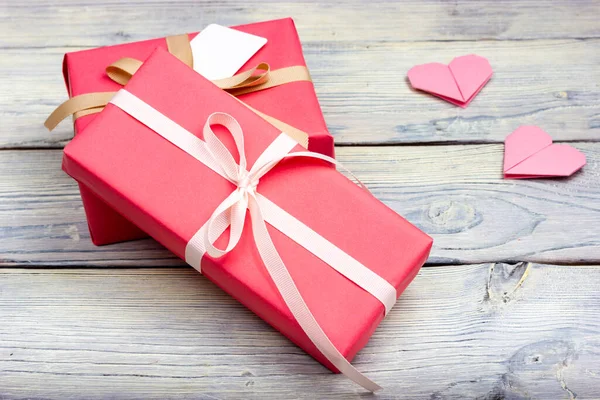 Διάφορα δώρα τυλιγμένα σε ροζ χαρτί και δεμένα με λευκή κορδέλα σε ανοιχτό ξύλινο τραπέζι. — Φωτογραφία Αρχείου