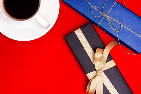 Cadeau noir avec ruban beige, cadeau bleu et une tasse de café sur fond rouge. — Photo