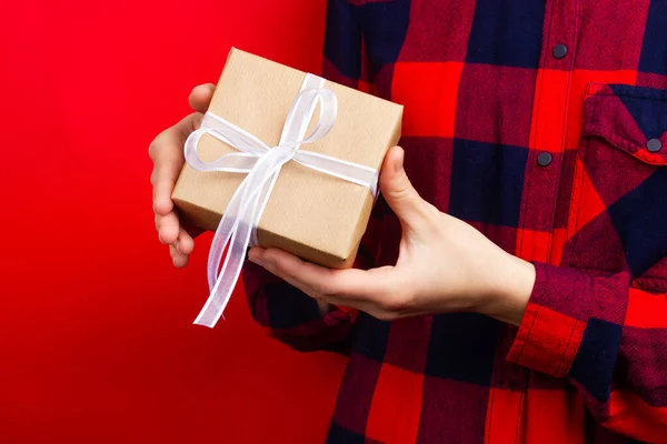 Uma rapariga de camisa vermelha tem um presente amarrado com uma fita branca. Preparando presentes para um ente querido. — Fotografia de Stock