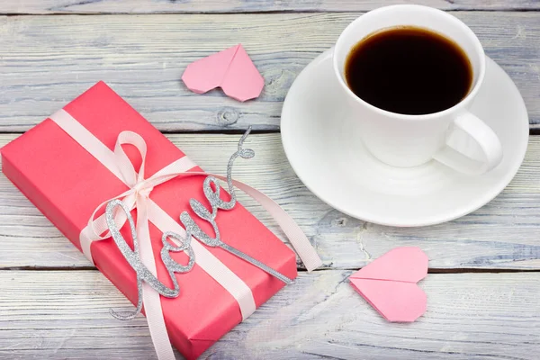 The gift is wrapped in pink paper, tied with a white ribbon, the words love and a cup of coffee on a light table. Provence style.