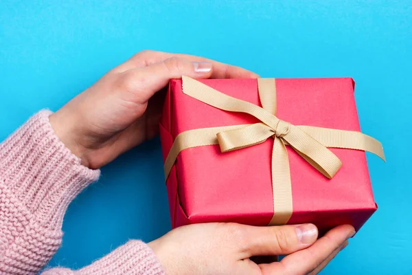 As mãos femininas mantêm um presente rosa amarrado com uma fita bege. O momento de dar um presente. — Fotografia de Stock