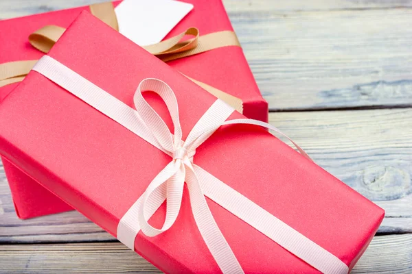 Deux coffrets cadeaux enveloppés dans du papier rose et attachés avec un ruban blanc sur une table en bois clair. — Photo