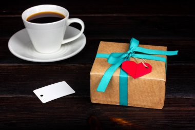 Bir fincan kahve ve koyu ahşap bir masada el işi kağıda sarılmış güzel bir hediye paketi. Kırsal biçim