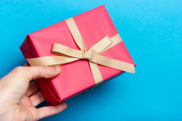 Cadeau rose dans une main féminine sur un fond bleu. Fille tenant une boîte cadeau enveloppée dans du papier rose. — Photo