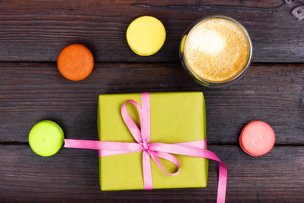 Krásná dárková krabice zabalená v zeleném papíru a malé francouzské makarónové sušenky na tmavém stole. Ploché — Stock fotografie
