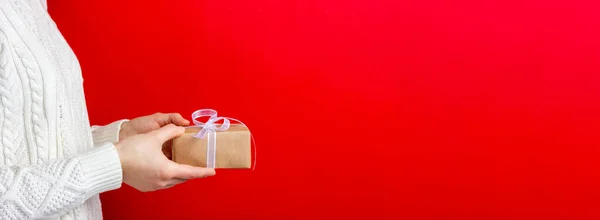 Caixa de presente em papel artesanal em mãos femininas. Fundo vermelho. Espaço publicitário — Fotografia de Stock