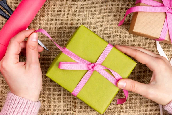 Processo de embrulho de presentes. As mãos femininas estão segurando um presente rosa. Festive Flat Lay. Vista de cima — Fotografia de Stock