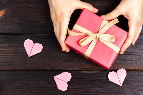 Female hands are holding a pink gift with a beige ribbon. Flat Lay gift. Gift giving, top view. — Fotografia de Stock