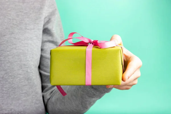 Uma mão feminina segura um presente verde com uma fita rosa. Parabéns pelo feriado. Feliz Aniversário. Dia dos Namorados. Presente de Natal. — Fotografia de Stock