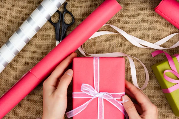 Processus d'emballage cadeau. Vue d'en haut. Les mains des femmes emballent une boîte-cadeau. Cadeau rose avec ruban blanc — Photo