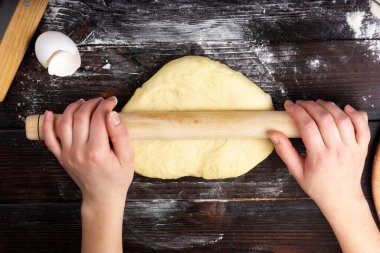 Dişi eller hamuru merdaneyle çeviriyor. Ekmek pişirmek için maya hamuru.