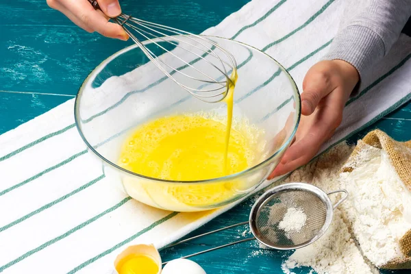 Womens hands beat eggs with a whisk. Beaten eggs in a glass bowl. The process of making pancake dough.