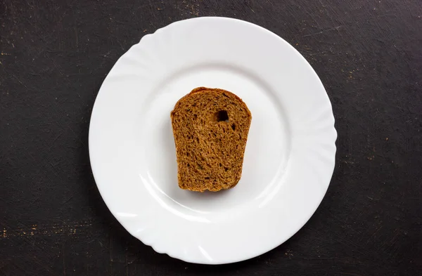 Una rebanada de pan de centeno en un plato blanco. Placa con pan sobre fondo negro. — Foto de Stock
