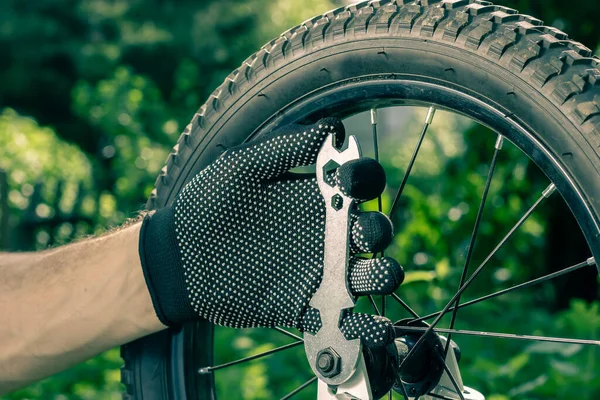 Reparación de bicicletas. Apretando la rueda de la bicicleta. Llave de bicicleta en la mano de un hombre. El maestro mantiene la moto. —  Fotos de Stock