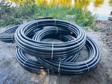 Sarılmış siyah plastik borular bir nehir kıyısının yakınına istiflenmiş. Yaratıcı ve ticari projeler için mükemmel.