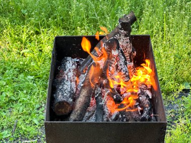 Kare ateş çukuru, yeşil çimenlikte yanan odunlar. Çok çeşitli kullanım alanları için uygun