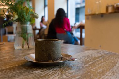 Kafedeki ahşap masada kahve fincanı, Bokeh arka planda bir kahve dükkanının atmosferi.