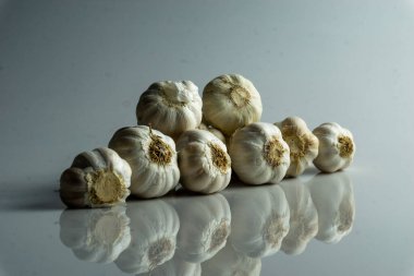 Beyaz arka planda bir grup çiğ sarımsak üst üste dizilmiş.