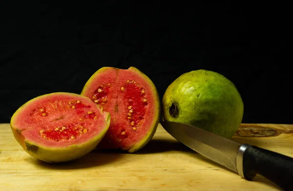 Guava fruit cut into pieces and kept on the table alongside a full guava fruit