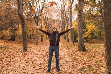 Beyaz adam sonbaharda parkta ağaç yaprağı fırlatma oyunu oynuyor.