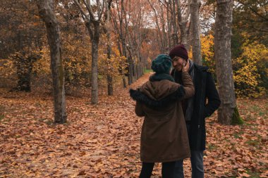 Tanımlanamayan yün şapkalı beyaz kadın sonbaharda parkta suç ortağı olan beyaz bir adama bakıyor.