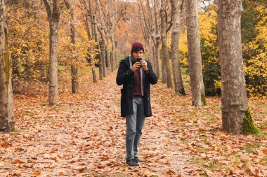 Doğada yürüyen beyaz bir adam sonbaharda bir cep telefonuna bakıyor.