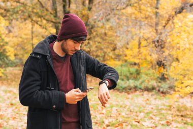 Parkta cep telefonuna bakan ve sonbaharda sıcak tutacak kıyafetleri olan akıllı bir adam.