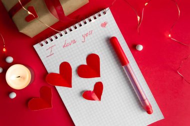 Kırmızı arka planda düz bir sevgililer günü kompozisyonu. Paketlenmiş hediye, metin için yer.