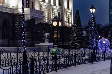 Şehir arkaplan gecesi Noel manzarası, şehir saati ve meydandaki çelenkli ışıklar.