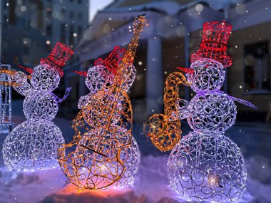 Kış şehri dekorasyonu. Gece manzarasının arka planında çelenk taşıyan kardan adamlar.