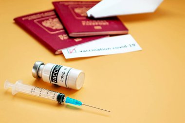Coronavirüs salgını sırasında seyahat konsepti. Turuncu arka planda Covid-19 aşısı ve turist pasaportu.