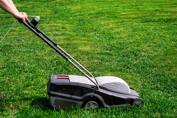 Work in the backyard of the house in the garden, mowing the lawn with an electric mower, the hands of the gardener in the frame, horizontal photo.